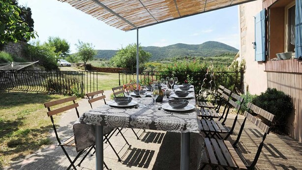Un espace de restauration en plein air avec une table dressée pour six personnes, entourée de bancs en bois, sous une pergola.