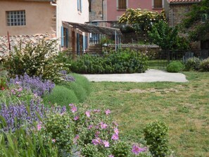 A garden with various plants and flowers, a pathway, and a building with a tiled roof. - Justine Oustalet (MONTGAILLARD)