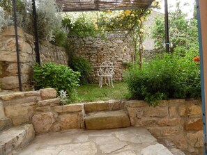 A stone wall garden with a metal chair and a pergola structure. - Justine Oustalet (MONTGAILLARD)