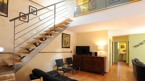 Un salon moderne avec un escalier, un canapé, deux fauteuils, un téléviseur et un meuble.