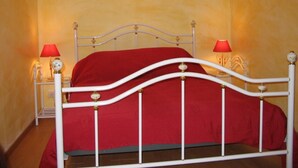 Un letto con struttura in metallo bianco e biancheria rossa, due lampade da comodino e un lampadario a parete.