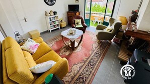 Ett vardagsrum med en soffa, fåtöljer, ett soffbord, en bokhylla, en tv och utsikt genom stora fönster.