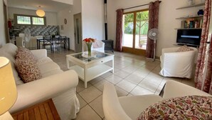 Un vaste salon meublé de blanc, avec un coin repas et une cuisine à l’arrière-plan.