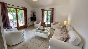 Un salon spacieux avec un canapé blanc, une table basse et un téléviseur posé sur une étagère.