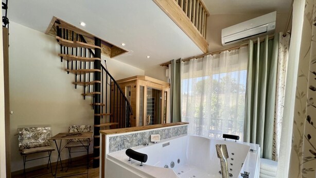 A modern bathroom with a freestanding bathtub, a wooden staircase, and a window with curtains. - Sous les Toits - Sauna & Balneotherapy (Canet D Aude)
