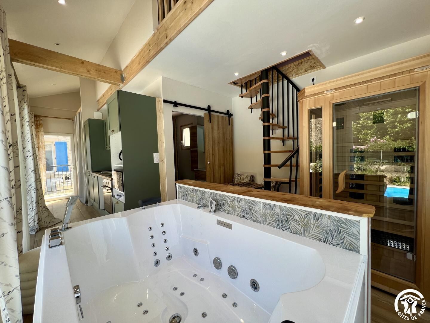 A modern bathroom with a large bathtub, wooden beams, and a glass door leading to a balcony.