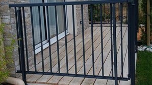 A balcony with a metal railing, a stone wall, and a view of a water tower in the background. - Sous les Toits - Sauna & Balneotherapy (Canet D Aude)