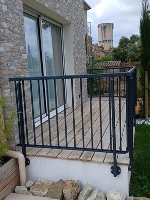 Un balcon avec une balustrade en métal, un mur en pierre et, au loin, une vue sur un château d’eau.