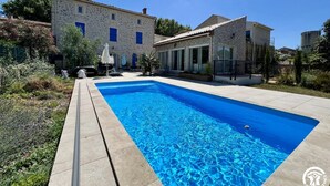A swimming pool with a stone house in the background. - Sous les Toits - Sauna & Balneotherapy (Canet D Aude)