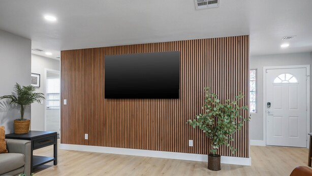 Un salon moderne avec un grand téléviseur à écran plat fixé sur un mur recouvert de panneaux en bois, un canapé, une table basse et une plante en pot.