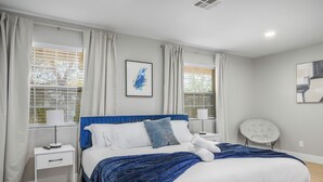 Une chambre moderne avec un grand lit, des tables de chevet blanches, une tête de lit bleue et une vue sur l’extérieur par les fenêtres.