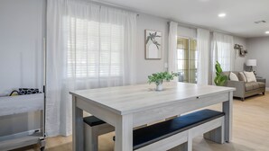Un salon moderne avec une table en bois de couleur claire, un banc et un canapé. On peut voir une plante en pot sur la table et une autre sur le canapé.