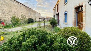 Un cortile con un muro in pietra, un piccolo giardino e un edificio con una finestra e una porta blu.