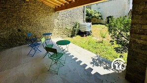 Patio esterno con parete in pietra, travi in legno a soffitto e tavolo con sedie.