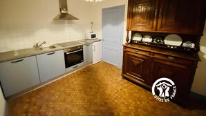 Una cucina compatta con microonde, forno e lavello. Si nota un mobiletto in legno con stoviglie e un lampadario.