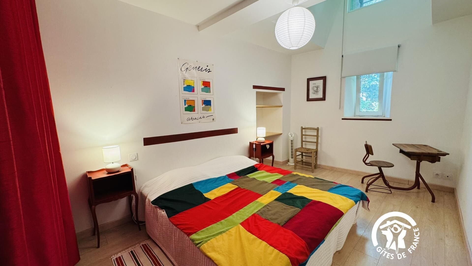 A bedroom with a bed, a nightstand, a chair, a small table, a window, and a wall with a poster.