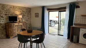 A dining area with a round table and chairs, a stone wall, a television on a wooden cabinet, and a view of a truck through a glass door. - Alice - MONTGAILLARD (MONTGAILLARD)