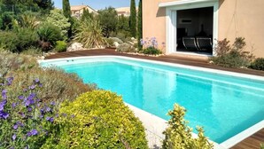 Une piscine entourée d’une végétation luxuriante et un bâtiment doté d’une terrasse.