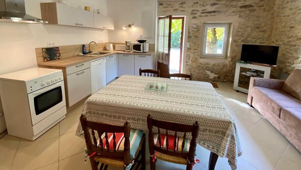Une cuisine compacte équipée d’une cuisinière, d’un four à micro-ondes et d’un évier. On y trouve une table à manger avec des chaises, ainsi qu’un téléviseur dans un espace de vie dont les murs sont en pierre.