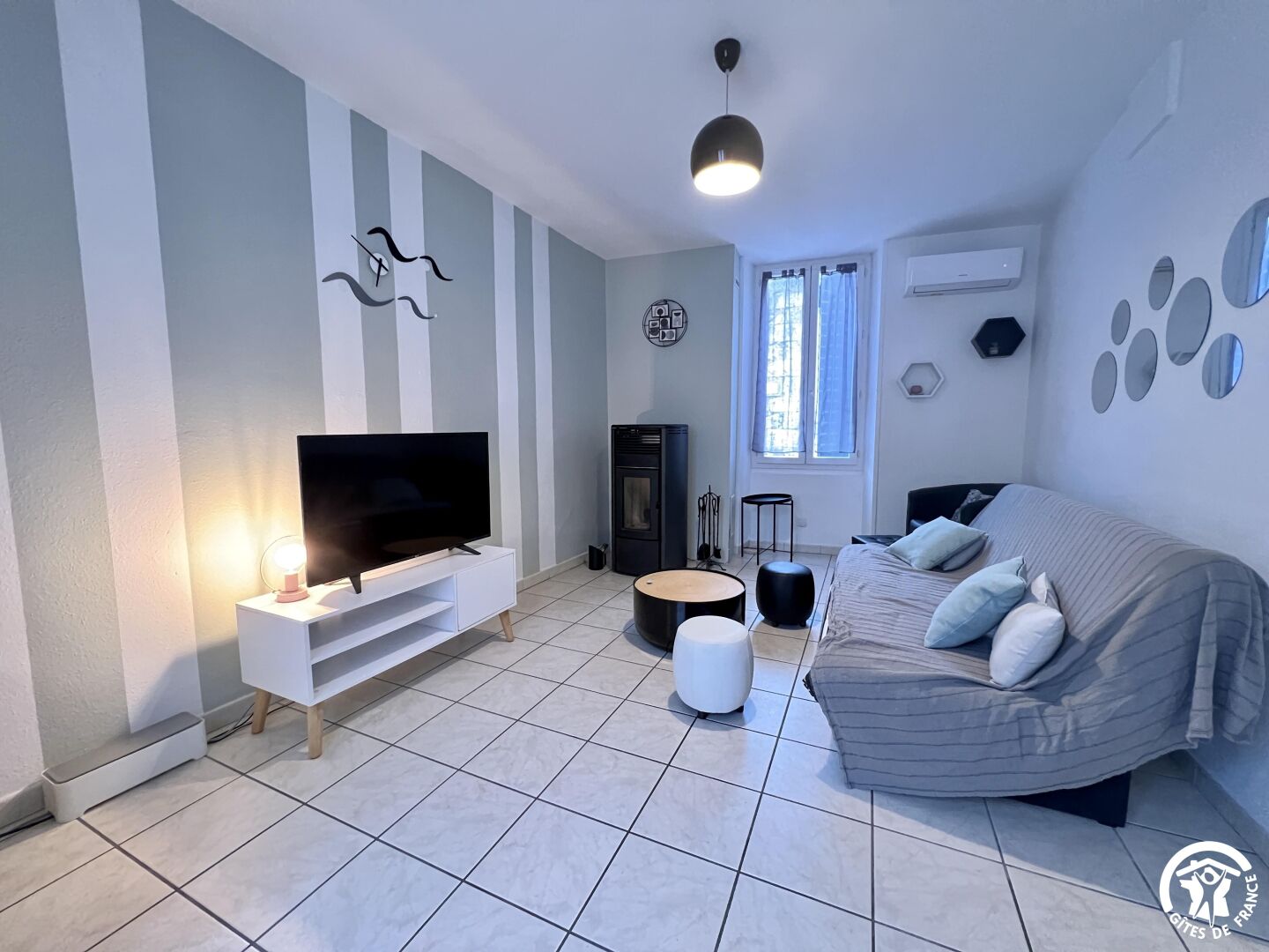 A modern living room with a flat-screen TV on a white TV stand, a sofa with cushions, a round coffee table, and a fireplace.