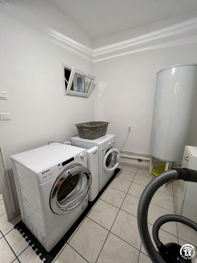 A laundry room with a Candy washer and dryer, a gray basket, a window, and a water heater.