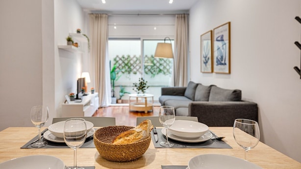 A dining area with a table set for two, a bowl of bread, and two wine glasses.