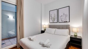 A hotel room with a bed, two bedside tables, a window with curtains, and two framed pictures on the wall.