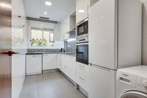 Une cuisine moderne avec des meubles blancs, un four encastré et un lave-vaisselle.