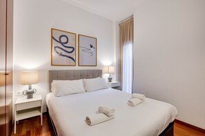 Une chambre d’hôtel avec un lit, deux lampes de chevet, une table de chevet et deux œuvres d’art abstrait accrochées au mur.