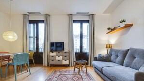 A modern living room with a sofa, TV, dining table, chairs, and a patterned rug. - Gran Via City Center Apartment (Barcelona)