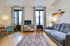 Ein modernes Wohnzimmer mit einer Couch, Fernseher, Esstisch, Stühlen und einem gemusterten Teppich.