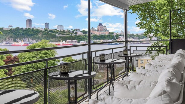 Ein Balkon mit Sitzgelegenheit im Freien, Blick auf einen Fluss und eine ferne Stadtlandschaft.