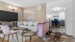 Ein modernes Wohnzimmer mit Flachbildfernseher, einer Couch, zwei Sesseln, einem Couchtisch und einer Wanddekoration.