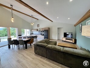 A modern living space with a dining area, sofa, TV, and kitchen. - Le Petit Gîte du Tatou (ROQUEFEUIL)
