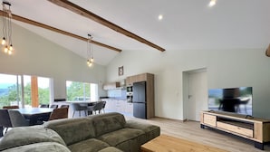 Una sala moderna con un sofá seccional, una mesa de centro de madera, un televisor y una cocina al fondo.
