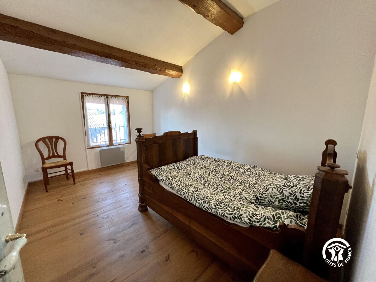 A bedroom with a wooden bed, a chair, a window with curtains, and a radiator.
