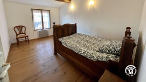 A bedroom with a wooden bed, a chair, a window with curtains, and a radiator. - La Bouriette - MOUSSOULENS (MOUSSOULENS)