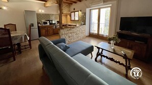 A cozy living room with a sofa, a television, and a kitchen area with a stone island. - La Bouriette - MOUSSOULENS (MOUSSOULENS)