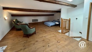 A loft bedroom with exposed wooden beams, a skylight, a bed, two chairs, and a small table. - La Bouriette - MOUSSOULENS (MOUSSOULENS)