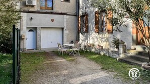 A two-story building with a garage door, a small balcony, and a garden area with a table and chairs. - La Bouriette - MOUSSOULENS (MOUSSOULENS)