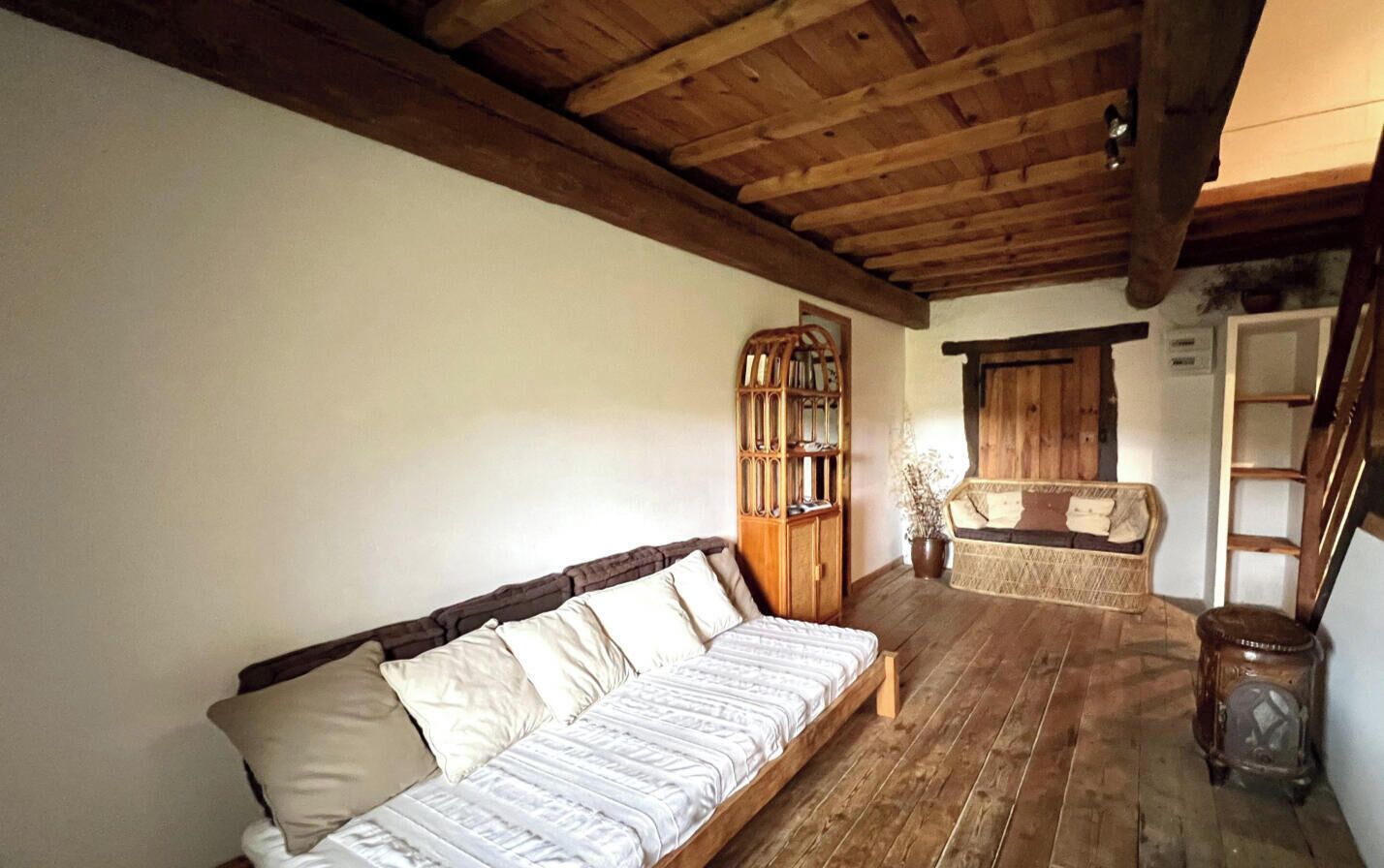 A room with a wooden ceiling, a sofa, a wicker chair, and a cabinet.