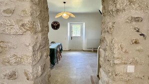 A stone-walled corridor leading to a dining area with a hanging light fixture and a door with a window. - Etoiles des Salins - Gîte 2 (PORT LA NOUVELLE)