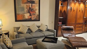 Uma sala de estar com um sofá cinzento, uma poltrona de couro marrom e um grande quadro abstrato na parede.