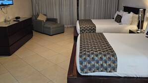 Quarto de hotel com cama, sof á, televisão e ventoinha no teto.