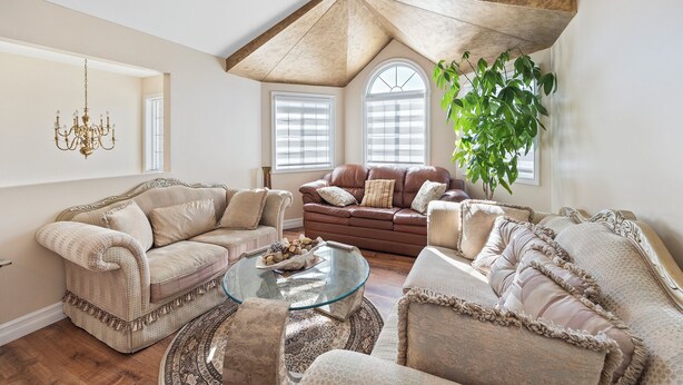 Una sala de estar acogedora con techo alto, un sofá de cuero marrón, sillones beige y una mesa de centro de vidrio.