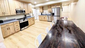 Eine moderne Küche mit Holzschränken, Edelstahlgeräten und einem dunklen Esstisch aus Holz.