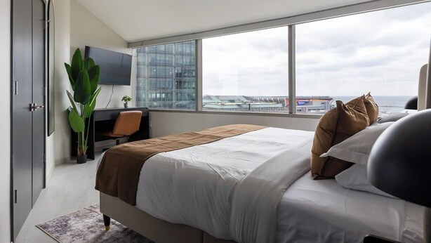A modern hotel room with a large bed, a desk, and a view of the city and water.