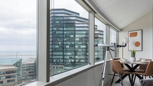A modern dining area with a panoramic city view, a telescope, and contemporary furniture.