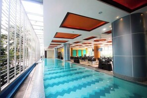 An indoor swimming pool with a blue patterned floor, surrounded by a glass enclosure with a view of greenery outside. - UPad Hotel (Manila)