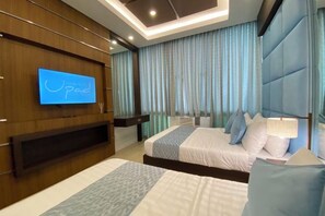 A hotel room with a TV on the wall, a bed with pillows, a bedside table, and a large window with curtains. - UPad Hotel (Manila)